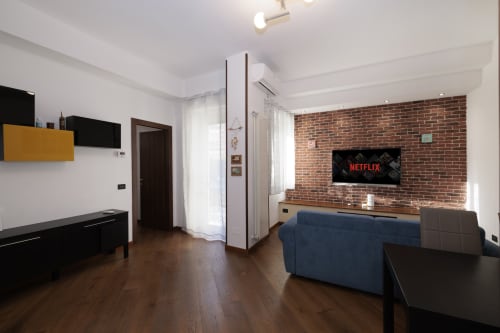 Modern living room with brick wall, flat-screen TV, blue sofa, wooden flooring at ViOletta apartment, Lido di Ostia