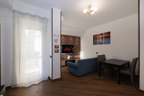 Modern living room at ViOletta apartment in Lido di Ostia with blue sofa, dining table, brick fireplace TV wall, and garden
