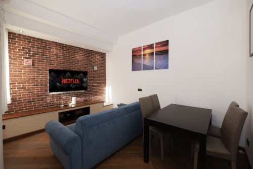 ViOletta CasettAmare apartment living area with blue sofa, dining table, brick fireplace wall with flat-screen TV showing