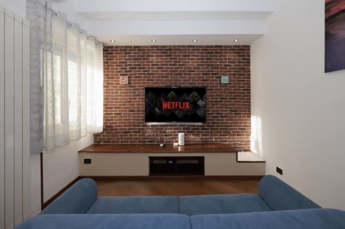 Modern living room with blue sofa, mounted TV showing Netflix on exposed brick wall, wooden furniture in ViOletta apartment,