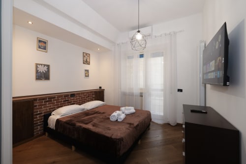 Modern bedroom at ViOletta apartment with brick headboard, brown bedding, flat-screen TV, and garden views in Lido di Ostia