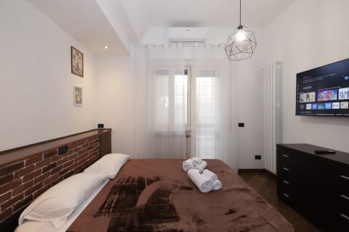 Modern bedroom at ViOletta hotel in Lido di Ostia with brick headboard, brown bedding, flat-screen TV, and geometric pendant