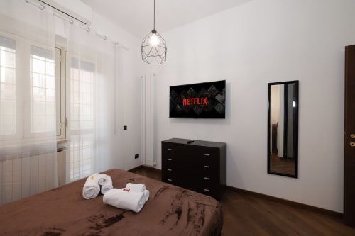 Modern bedroom at ViOletta hotel in Lido di Ostia with brown bed, black dresser, wall-mounted TV, geometric pendant light,