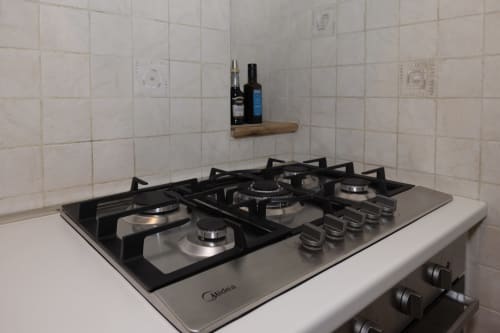 Midea gas cooktop with four burners in CasettAmare apartment at ViOletta, Lido di Ostia, with tiled backsplash and shelf