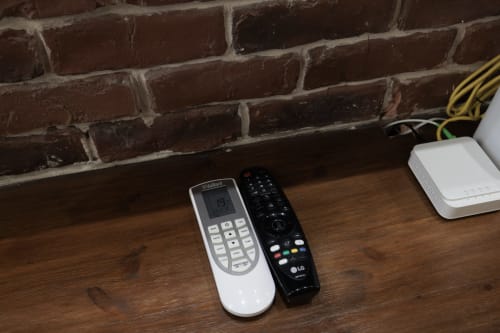 Two remote controls on wooden shelf at ViOletta apartment, Lido di Ostia, with brick wall and WiFi device in background
