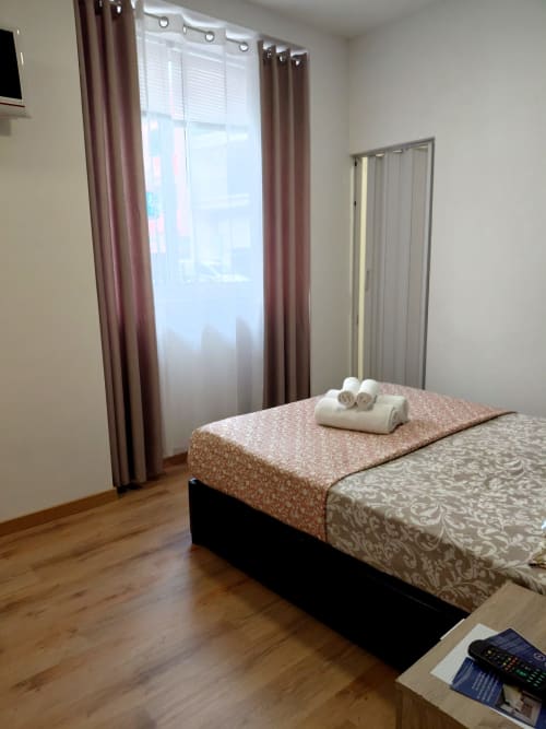 Quarto moderno do hotel Madeirarooms em Funchal com vista da cidade, cama com toalhas enroladas, cortinas marrom e piso de madeira.