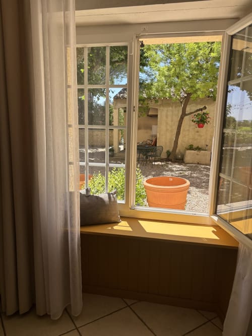 Portes vitrées ouvertes de la chambre Mimosa donnant sur la cour-jardin avec arbre et jardinière orange au Mas des Vignes, Rochegude