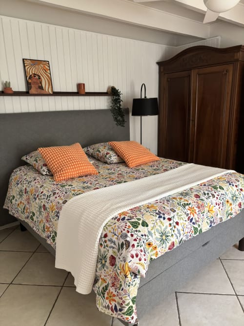 Chambre Mimosa au Mas des Vignes, Rochegude : lit avec parure florale, coussins orangés, tête de lit grise, armoire en bois