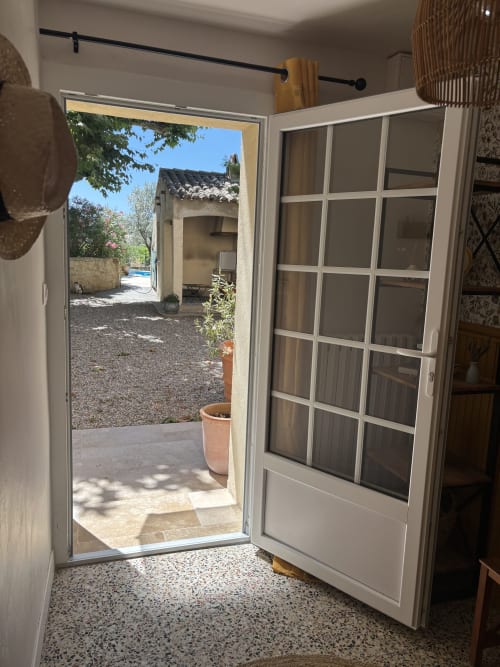 Chambre Mimosa avec vue sur le jardin au Mas des Vignes, Rochegude. Portes ouvertes sur la cour avec pot en terre cuite et allées en pierre.