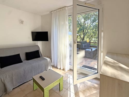 Chambre moderne à LOCADIGNE Digne-les-Bains avec canapé, TV, table verte et balcon vue montagne