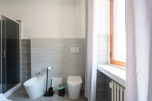 Bagno moderno a Centrale Bologna con wc, bidet e pareti piastrellate, dettagli in legno caldo e luce naturale