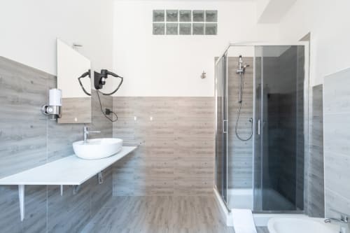 Bagno moderno nella BnB Centrale Bologna con lavabo bianco, doccia con box in vetro e piastrelle con effetto legno