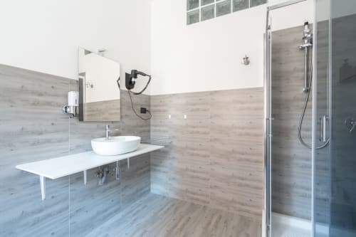 Bagno moderno dell'hotel Centrale Bologna con rivestimenti effetto legno, lavabo a bacinella e doccia walk-in in vetro