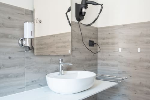 Bagno moderno con lavabo bianco a coppa, rubinetto cromato, rivestimento a effetto legno e soffione nero a parete presso Centrale