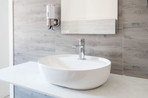 Lavabo tondo bianco moderno con rubinetto cromato nel bagno dell'hotel Centrale di Bologna con pareti in piastrelle effetto legno