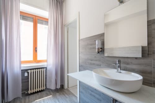 Bagno moderno dell'hotel Centrale Bologna con lavabo ovale bianco, mobile in legno scuro, rivestimento in piastrelle grigie e vista sulla città
