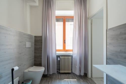 Bagno moderno a Centrale Bologna con piastrelle effetto legno, toilette, radiatore e grande finestra con cornice arancione