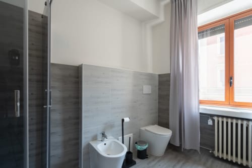 Bagno moderno dell'hotel Centrale Bologna con piastrelle grigie, sanitari bianchi, cabina doccia in vetro e finestra in legno