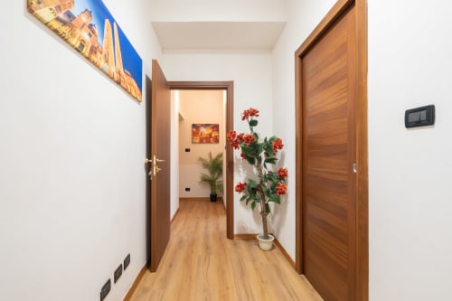 Moderno corridoio della Centrale Bologna B&B con porte in legno, pareti bianche e fiori rossi in vaso