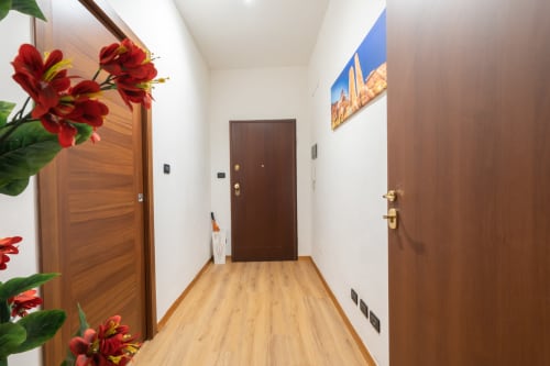 Luminoso corridoio in B&B a Bologna con porte in legno, fiori rossi e pavimentazione in legno chiaro