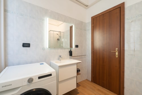 Bagno moderno alla Centrale Bologna con lavatrice, lavabo, specchio e porta in legno nella camera 28