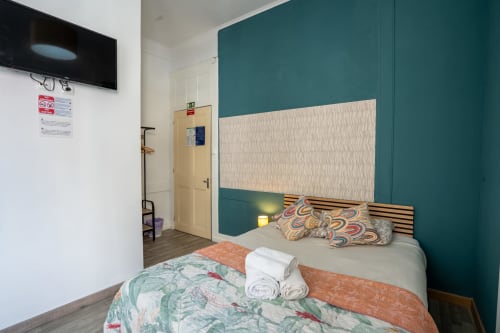 Quarto moderno do Madeirarooms Funchal com parede de destaque azul-petróleo, cama de madeira e vista da cidade pela janela