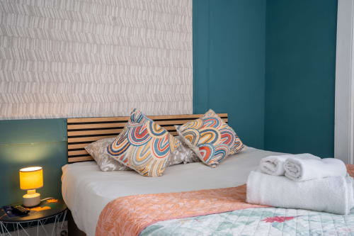Quarto moderno em Madeirarooms em Funchal com cama, almofadas coloridas estampadas, toalhas brancas e detalhes em azul-petróleo