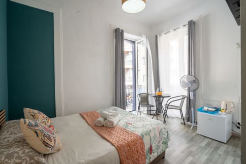 Quarto luminoso do Madeirarooms Funchal com vista para a cidade, cama, área de estar e parede de destaque em tons de azul-petróleo