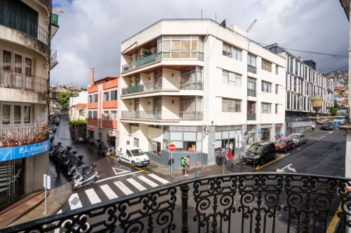 Vista da cidade do hotel Madeirarooms em Funchal, Portugal mostrando cruzamento de ruas com edifício branco e arquitetura local
