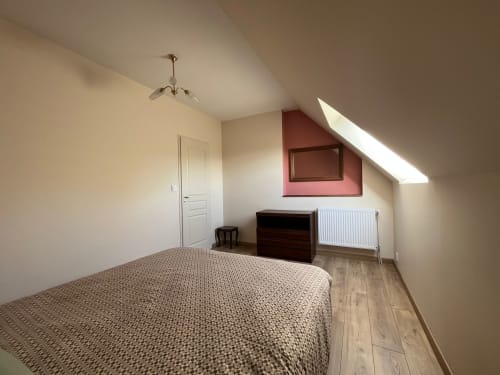 Chambre lumineuse sous les toits au Verger en Auge avec lit, coffre en bois, radiateur et fenêtre de toit