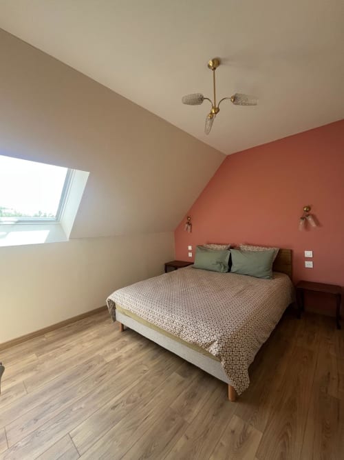 Chambre lumineuse sous les combles du gîte Le Verger en Auge avec lit queen-size, mur d'accent terracotta, lucarne et luminaire en laiton