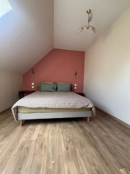 Chambre moderne à la Cabane Le p'tit verger, au Verger en Auge : plafond mansardé, mur accent rouge et parquet en bois