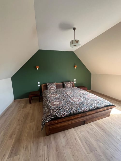 Chambre douillette sous les toits du gîte Le Verger en Auge avec lit en bois, mur d'accent vert et vue sur le jardin