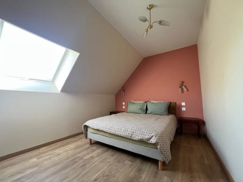Chambre mansardée du gîte Le Verger en Auge avec plafond incliné, lucarne, mur accent corail et parquet