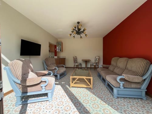 Spacieux salon du cottage Le Verger en Auge avec mobilier rayé, téléviseur, mur d'accent rouge et vue sur le jardin