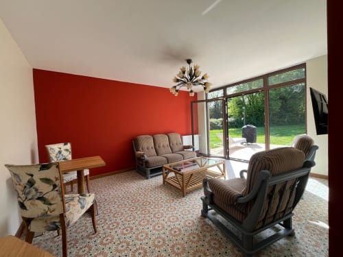 Séjour lumineux du Verger en Auge avec mur d'accent rouge, fauteuils rayés, TV et vue sur le jardin par la terrasse