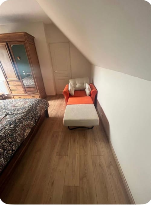 Chambre mansardée avec fauteuil orange, armoire en bois et lit à motifs du gîte Le Verger en Auge en Normandie