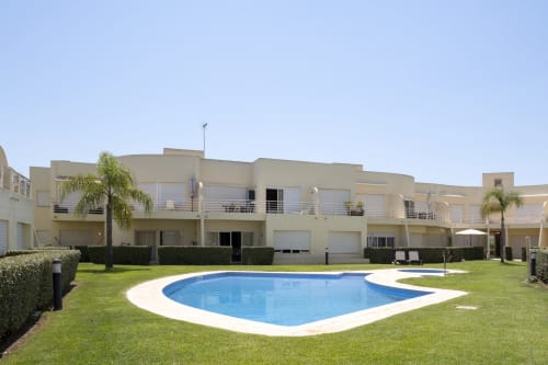 RB Algarve apartment complex in Vilamoura with kidney-shaped pool, manicured lawn, and modern terracotta buildings.