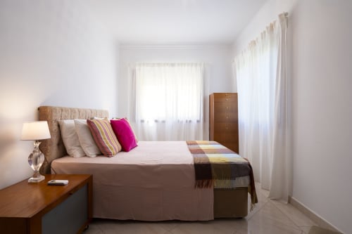 Bright bedroom at RB Algarve Vilamoura with queen bed, colorful pillows, wooden nightstand, and sheer curtains in Portugal