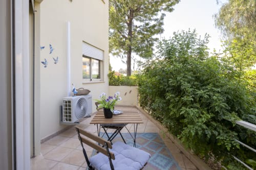 Cozy terrace at RB Algarve Vilamoura apartment with dining table, purple flowers, air conditioning unit, and lush green
