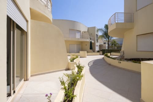 Modern apartment courtyard at RB Algarve Vilamoura with curved cream-colored buildings, palm trees, and sunny terrace area