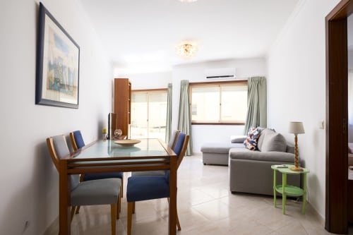 Modern apartment living room with dining table, grey sofa, and pool view at RB Algarve Vilamoura, Portugal