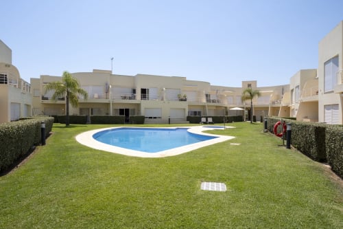 RB Algarve Vilamoura: modern beige apartment complex with shared pool, lush gardens, and palm trees in Portugal