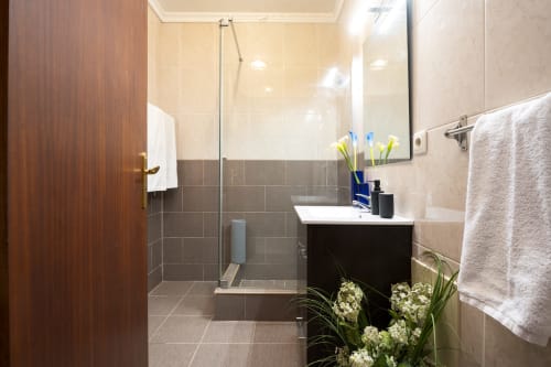 Modern bathroom in CRIS Vilamoura apartment at RB Algarve with shower, vanity, mirror, and decorative flowers