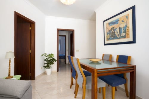 Modern dining area in CRIS apartment at RB Algarve Vilamoura with wooden table, blue and orange chairs, and artwork on white