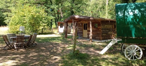 Chaumière rustique en bois rond de la Chambre d'hôtes Les Tramois à Donzy, avec espace de détente jardinet et vieille roue de charrette
