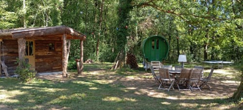 Installation de camping en forêt au gîte Les Tramois à Donzy avec caravane verte, cabane rustique et salon extérieur