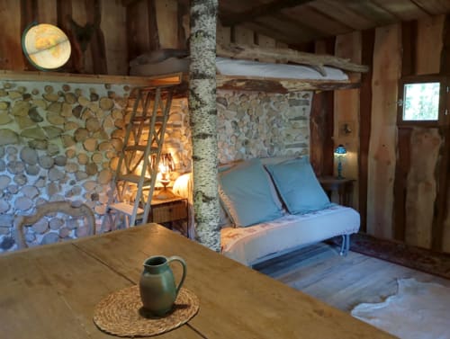Intérieur rustique du gîte Les Tramois à Donzy avec canapé bleu, poteau en bouleau et murs en pierre