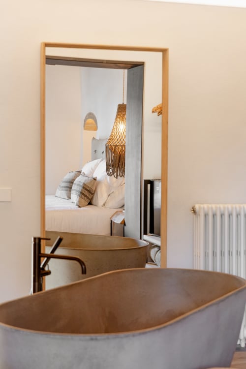 Reflejo en espejo del dormitorio del hotel Mas Escarrà mostrando cama con colgante de macramé y bañera moderna del baño al frente