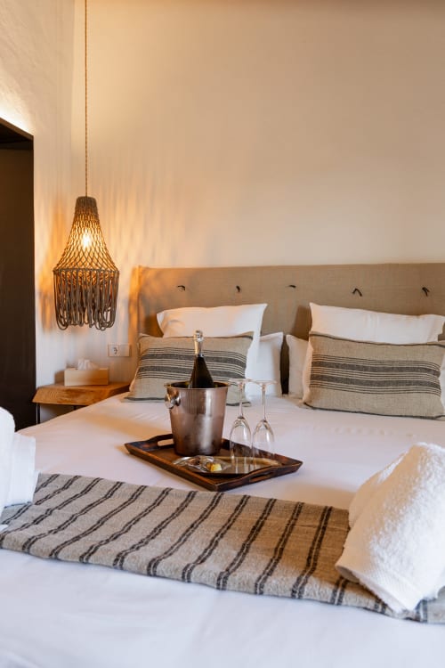 Elegante habitación del hotel Mas Escarrà en Caldes de Malavella con cabecero beige, almohadas a rayas, lámpara colgante y vino